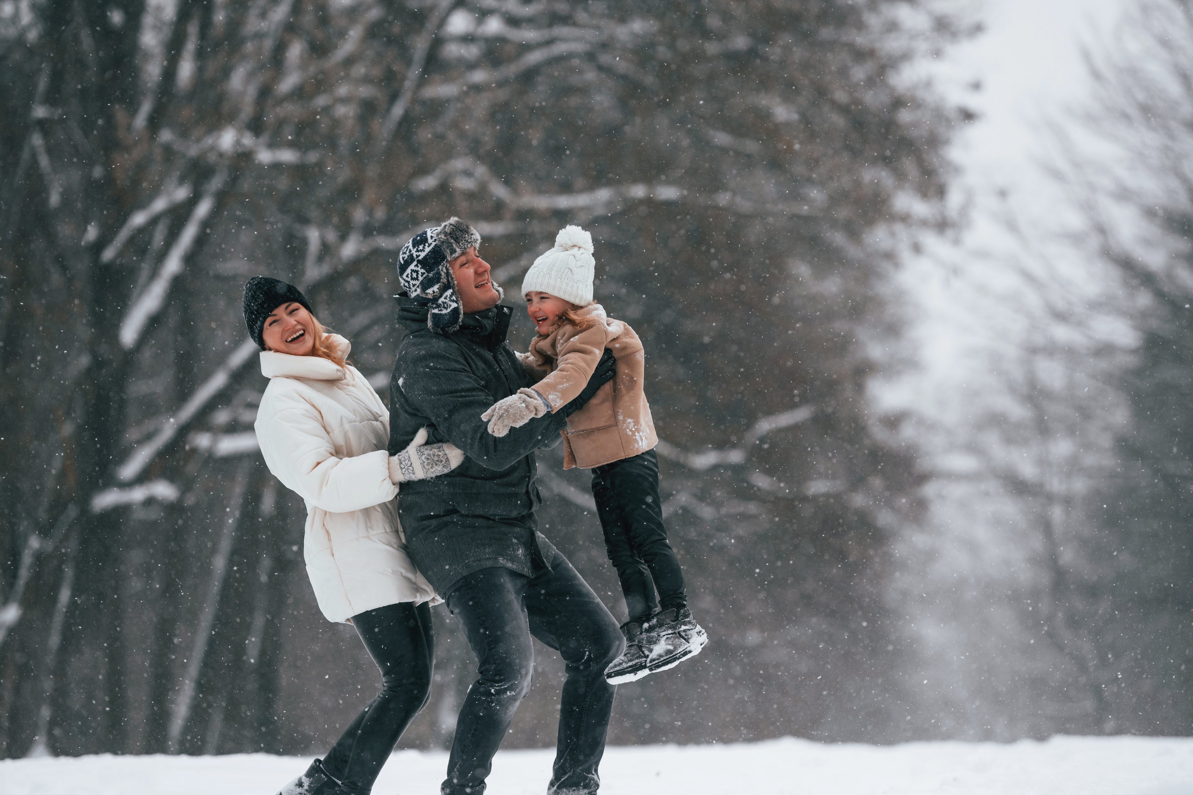Two adults and a child playing in the snow with trees in the background