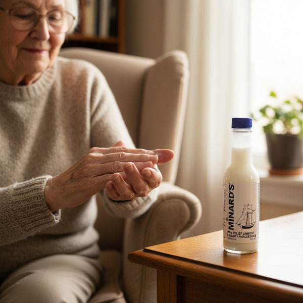 Senior woman applying lotion to her hand with a bottle of Minard's lotion on a table.
